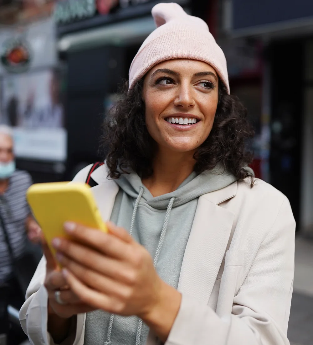 Frau schaut lächelnd auf ihr Smartphone in der Stadt